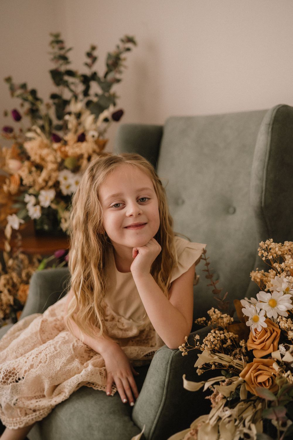 Whimsical portrait surrounded by dried floral arrangements in a sage green armchair.