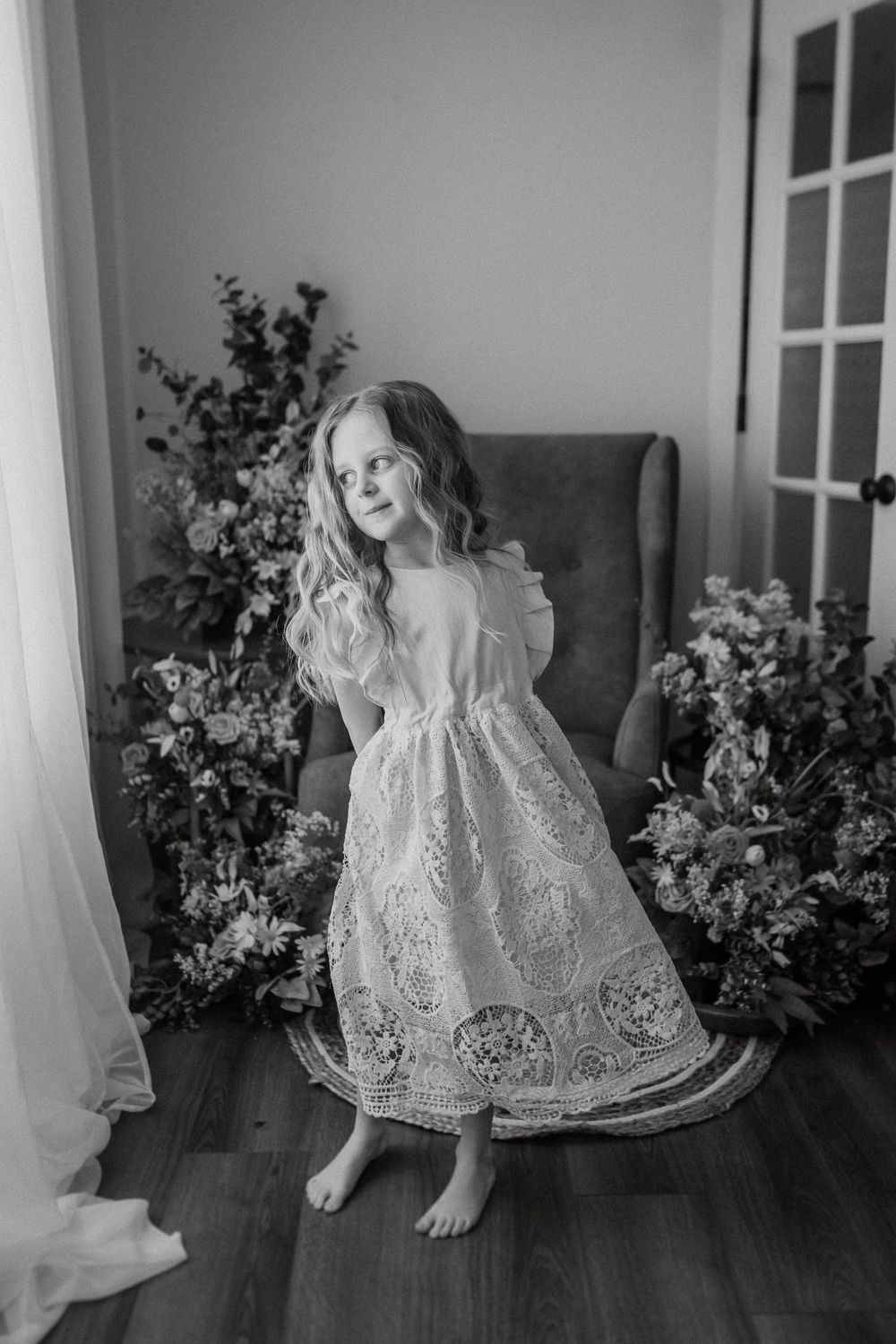 Artistic black and white portrait of a young dancer in a white lace dress twirling in a room decorated with flowers.