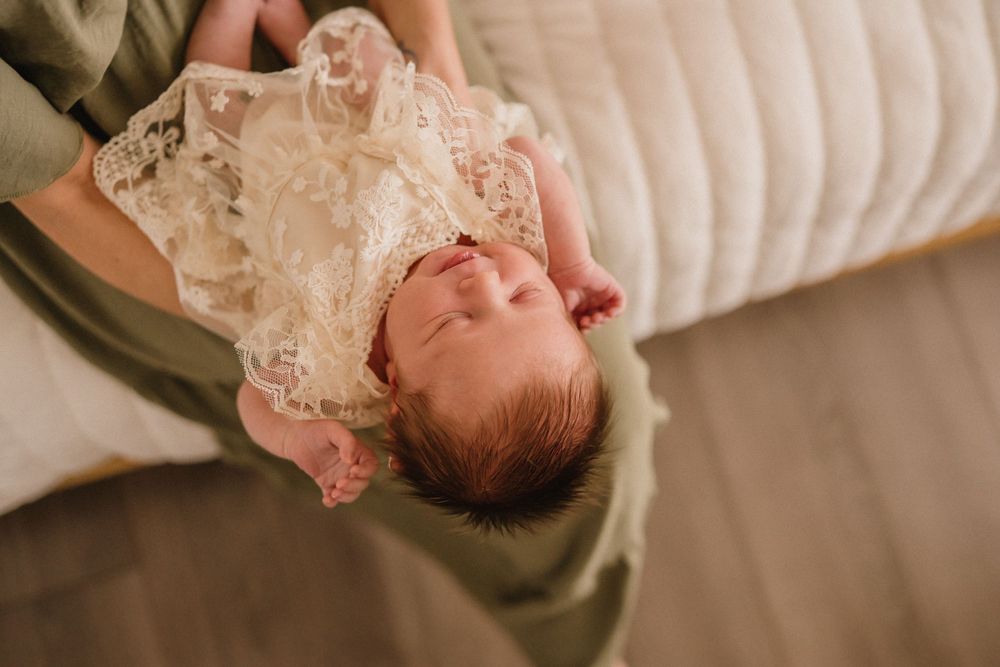 Newborn baby wrapped in delicate lace fabric lying on soft textured bedding in natural light.