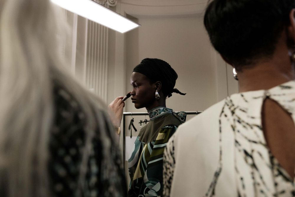 Candid backstage fashion show moment with stylists working on final touches.