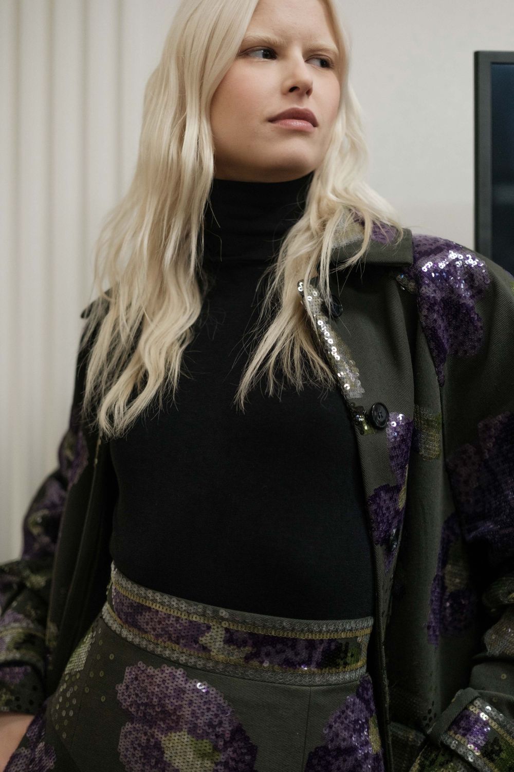 Model showcasing a black turtleneck with sequined military-style jacket.