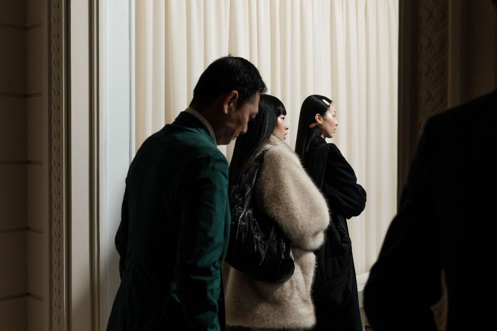 Models waiting in line against white curtain backdrop during fashion event.