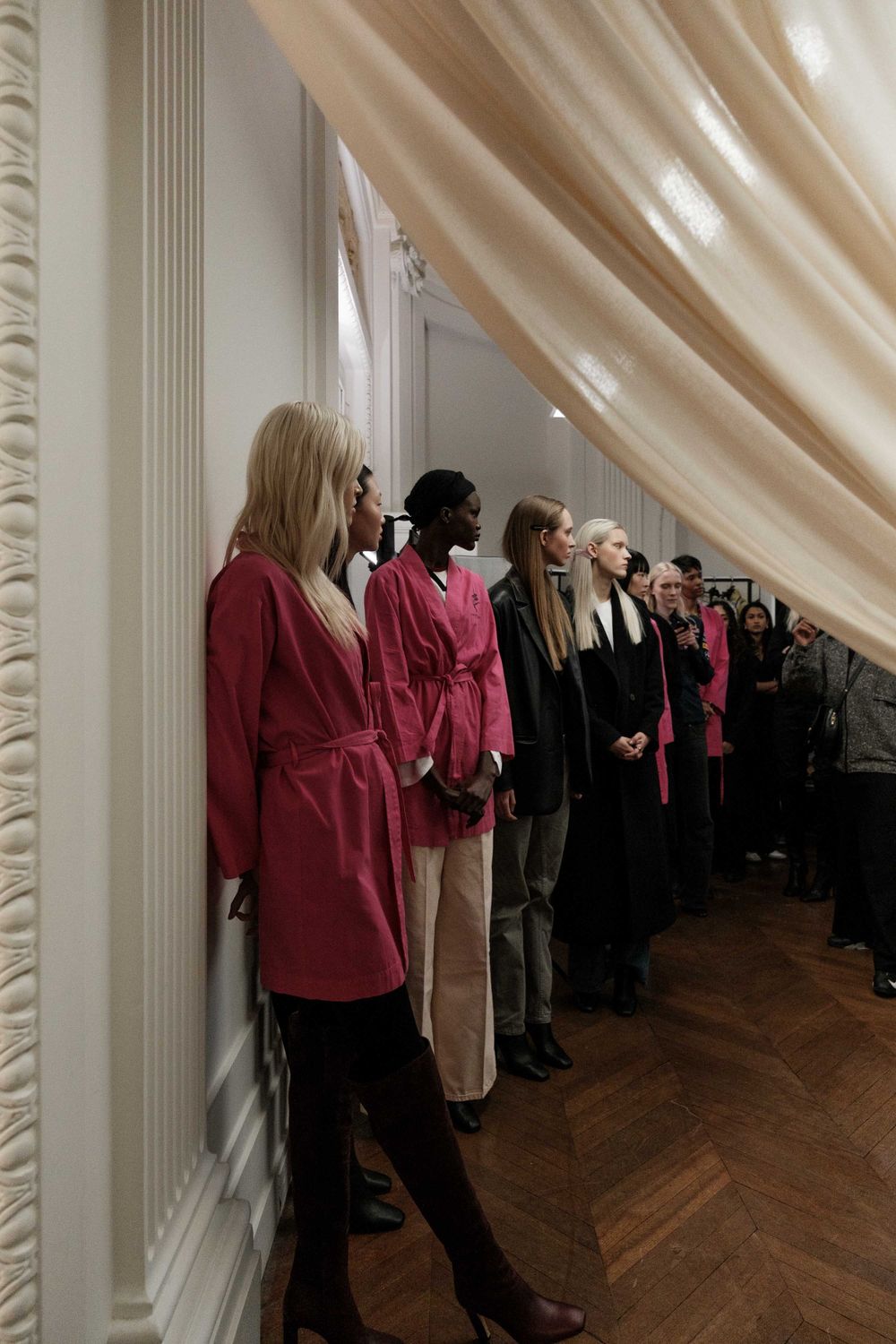 Models lined up against wall wearing red and black outfits during fashion presentation.