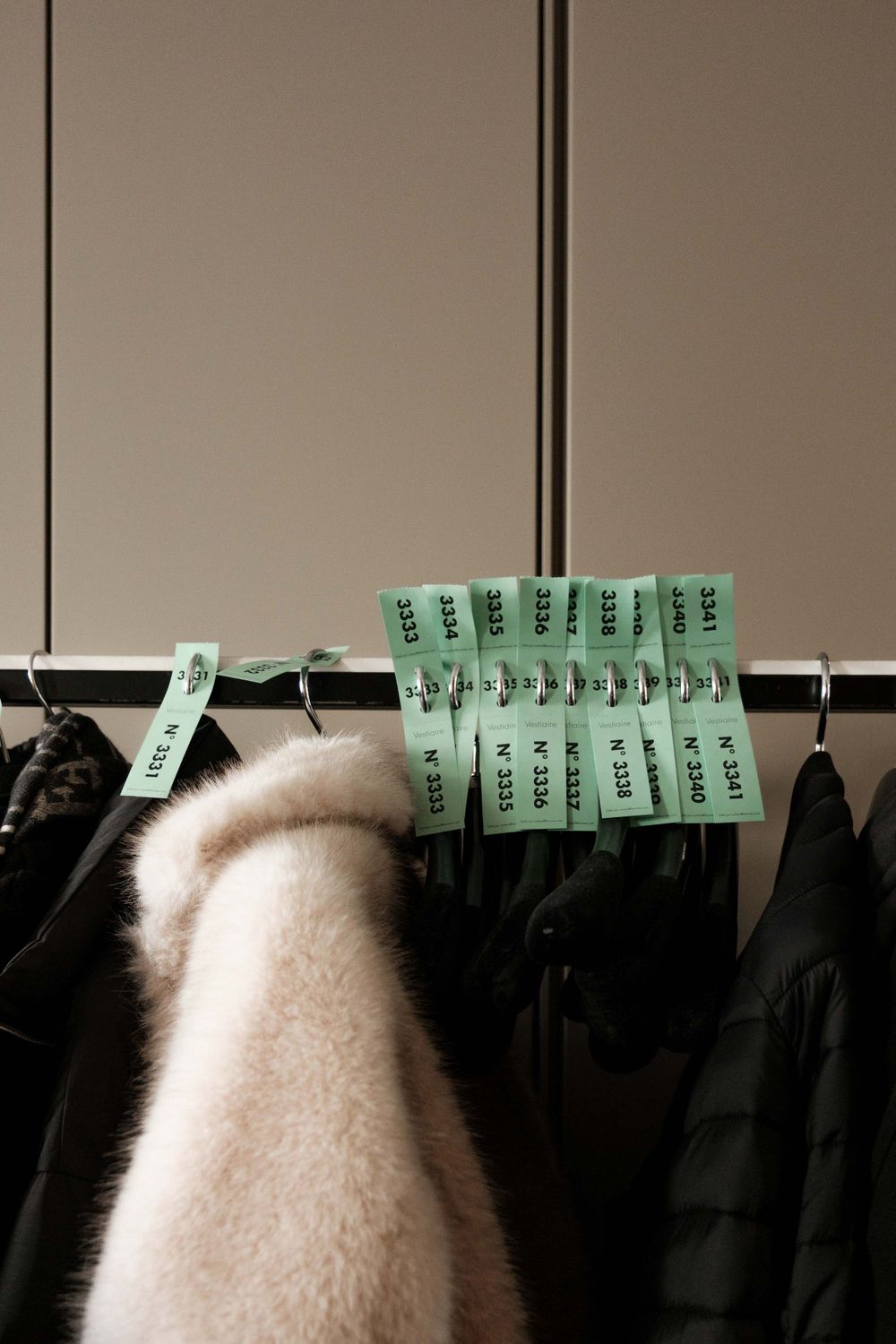 Green wardrobe tags hanging on a rack of dark clothing in a dressing area.