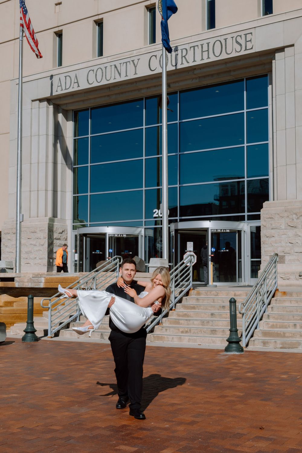 A couple poses romantically in front of the Ada County Courthouse building entrance with brick pavers and stone details.