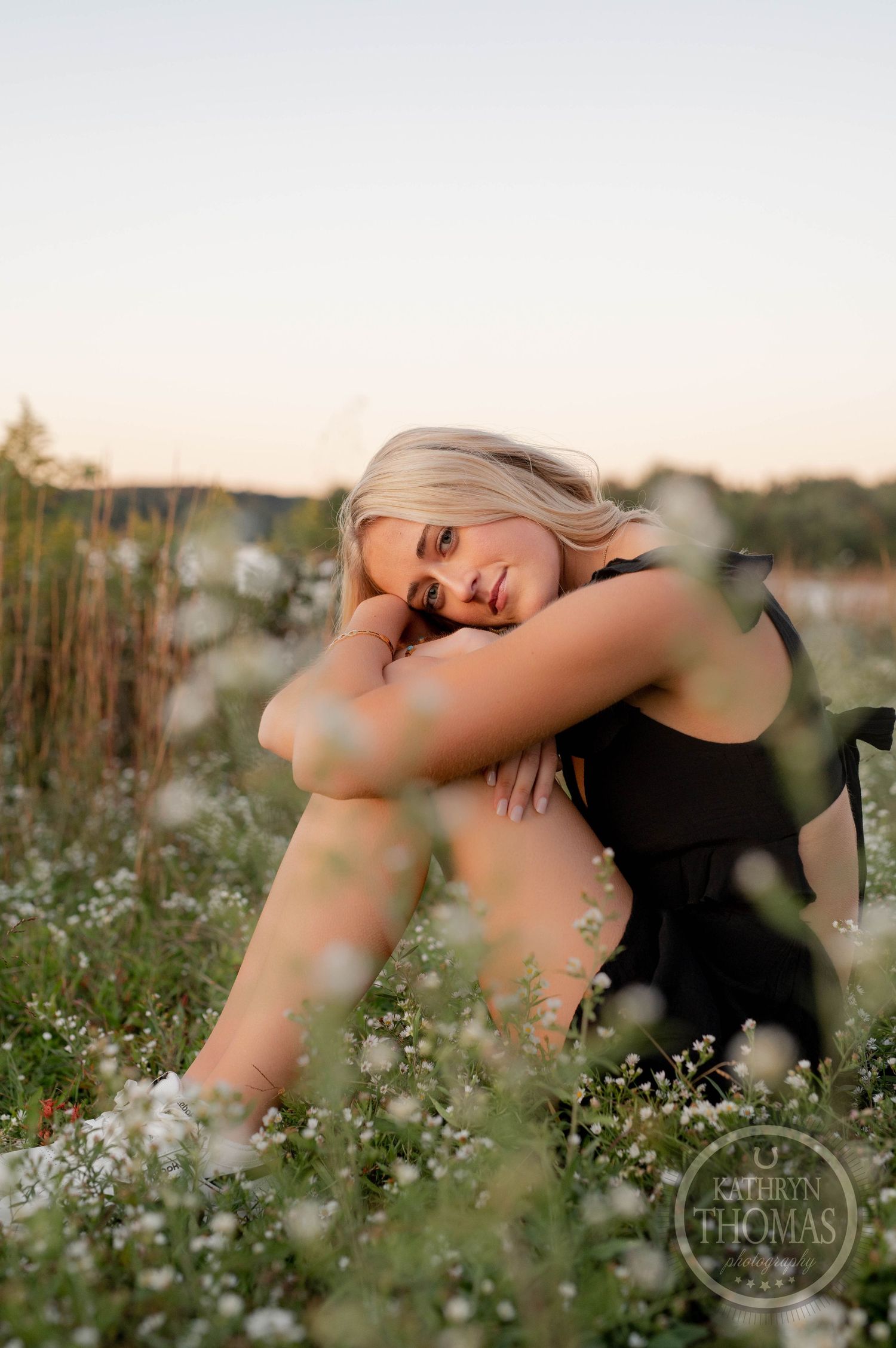 Dreamy sunset portrait in a field of delicate white wildflowers near water.