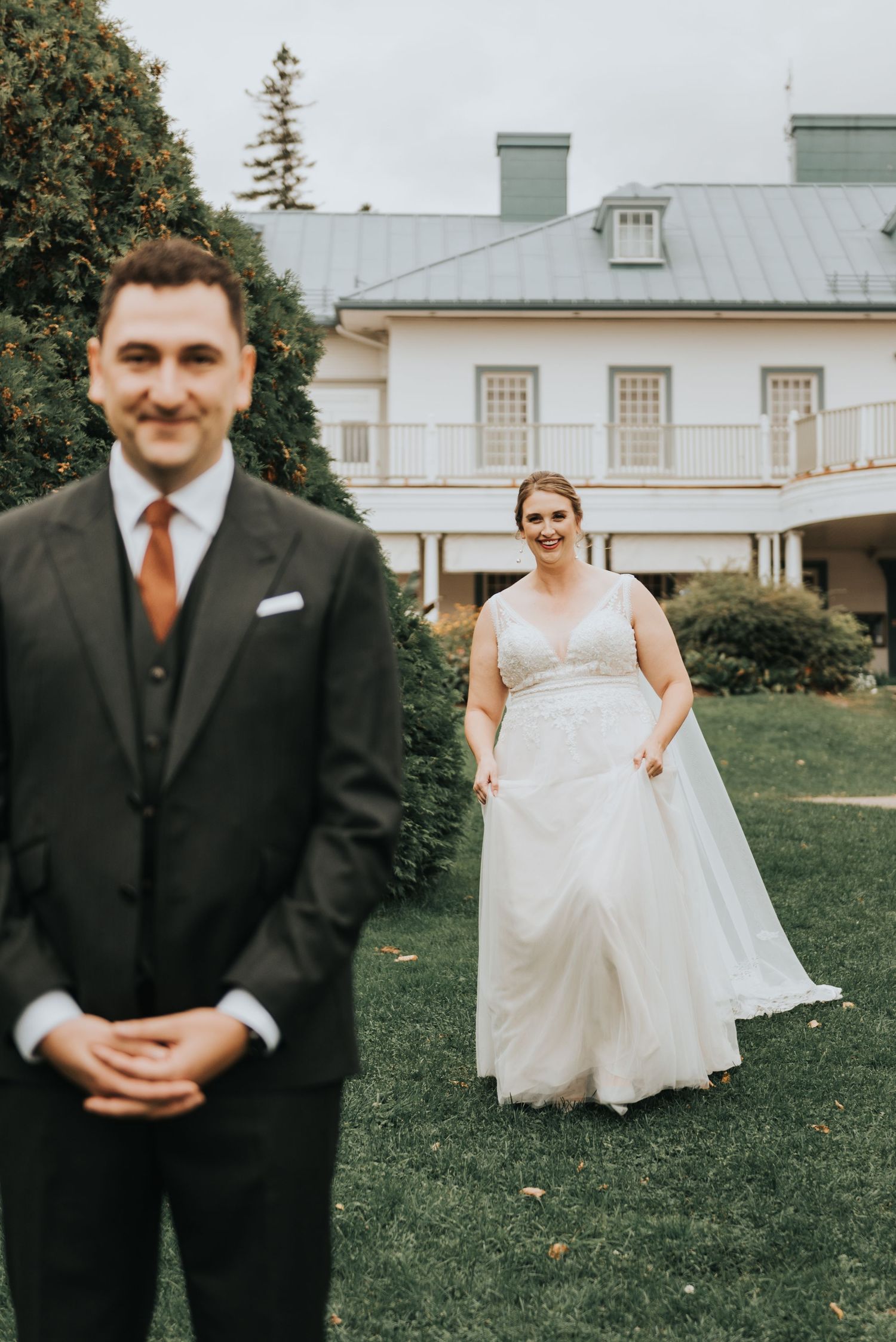 Newlywed couple at first look photograph on their wedding day in front of elegant white mansion with green lawn.