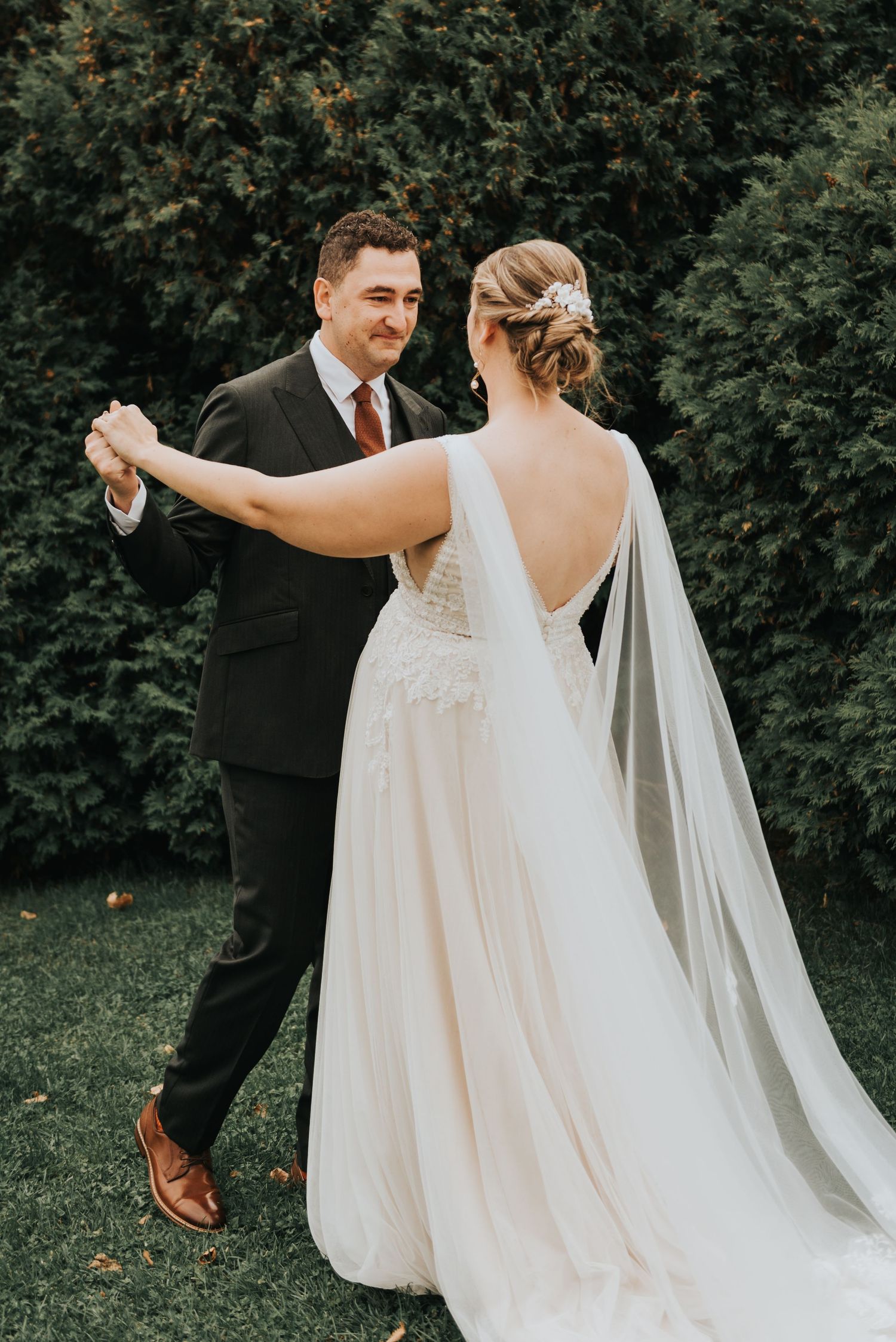 A couple shares their first dance together at their outdoor wedding, with the bride wearing a flowing white gown with veil.