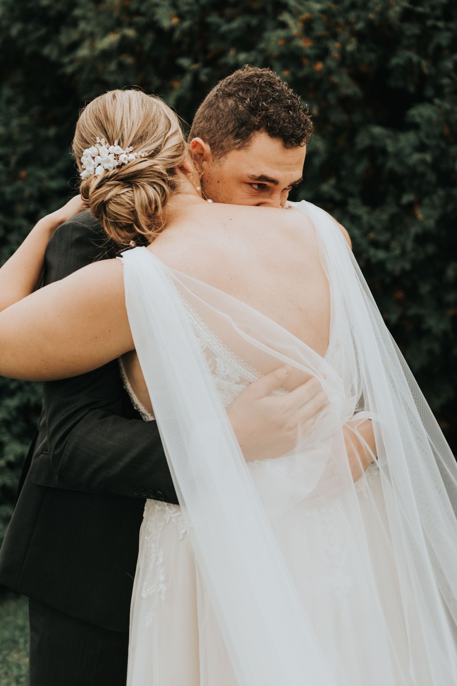 A tender moment between newlyweds embracing outdoors, with the bride wearing a flowing white veil and elegant updo.