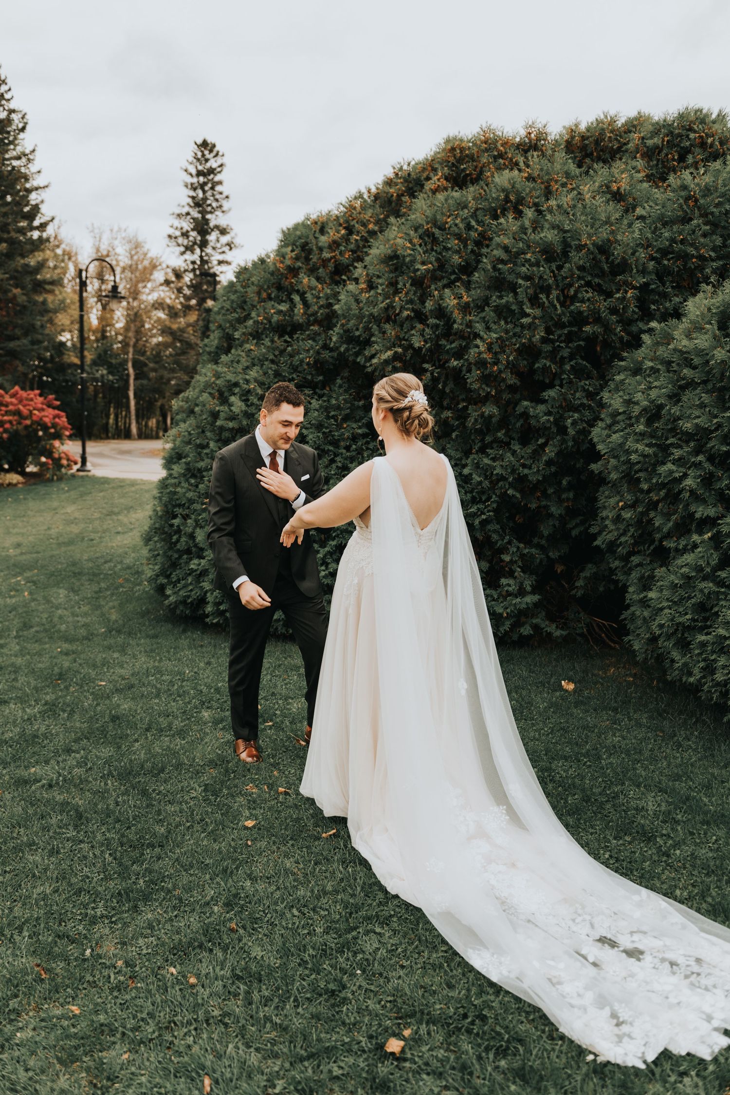 A couple shares a special moment in a garden setting with lush hedges, the bride wearing a flowing white dress with long veil.