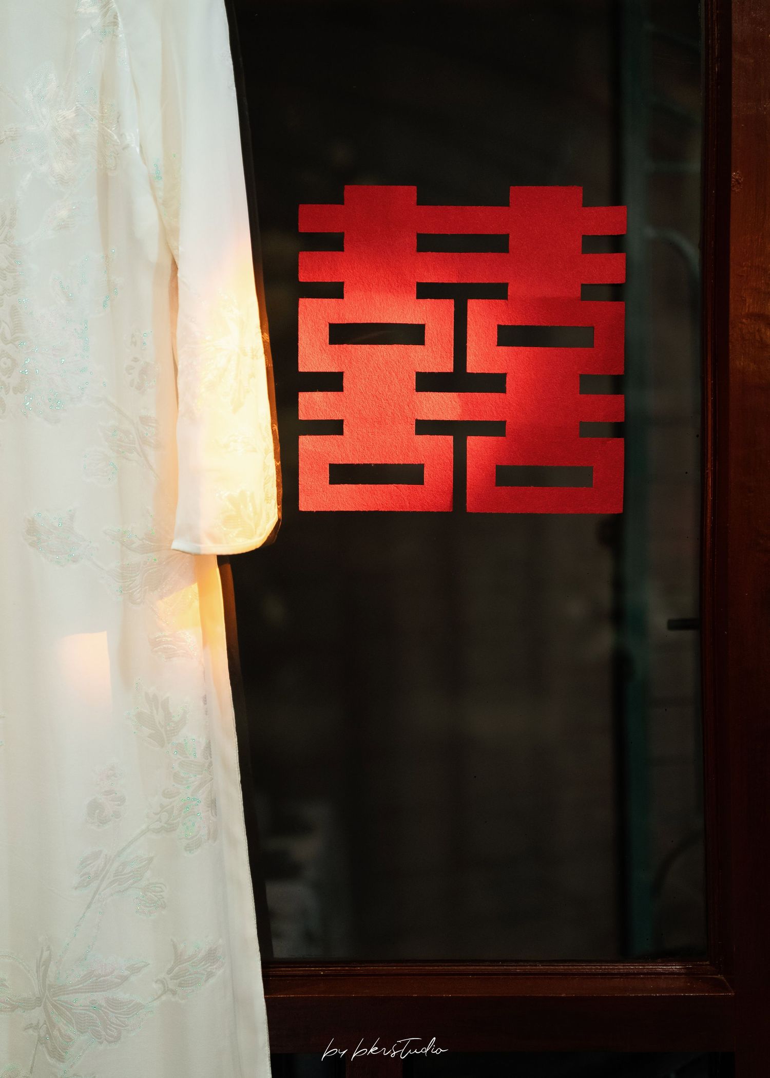Traditional Chinese double happiness symbol glows in red against a dark window with white curtain.