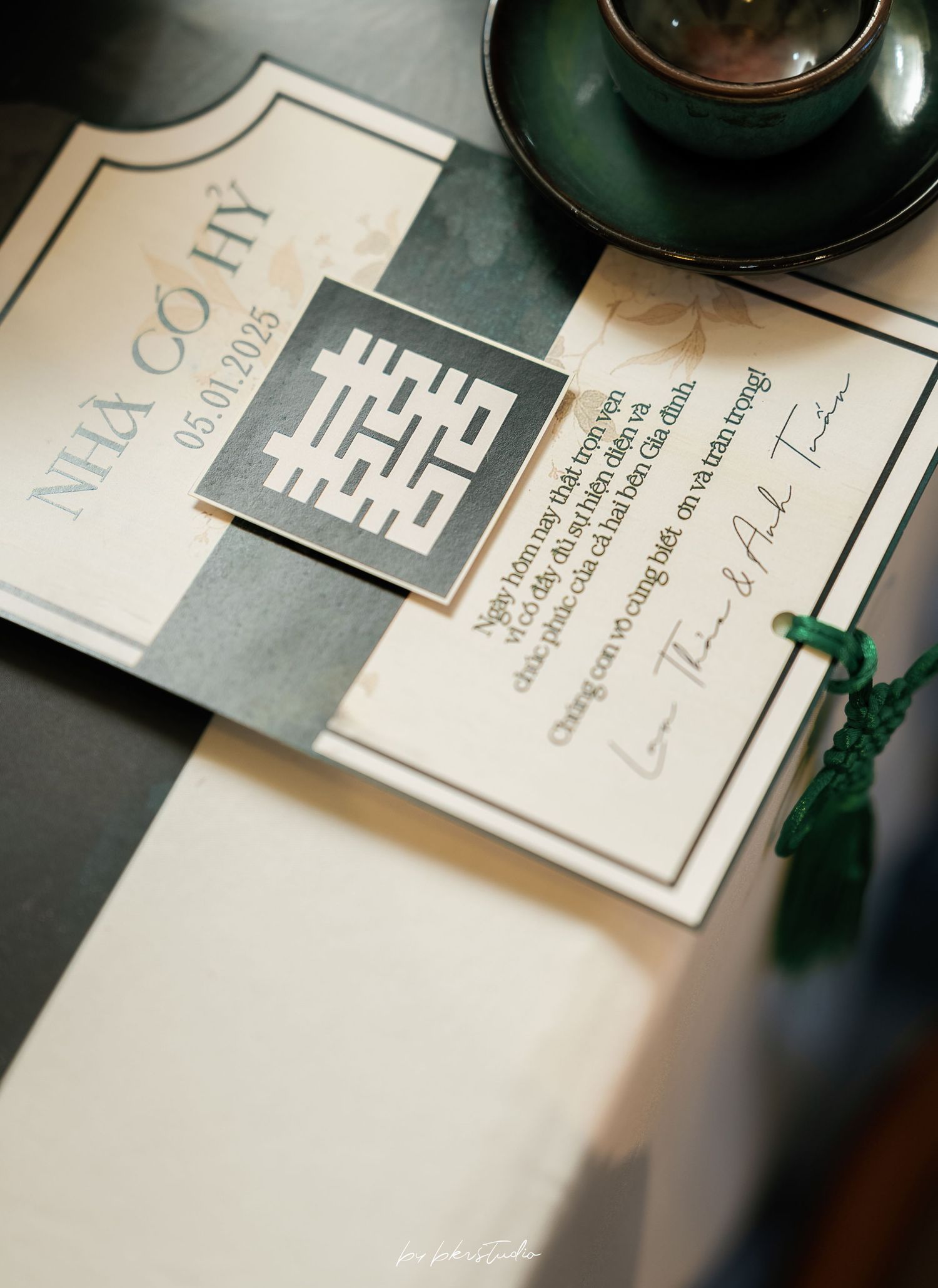 Wedding invitation cards with double happiness symbol and a green teacup on dark surface.