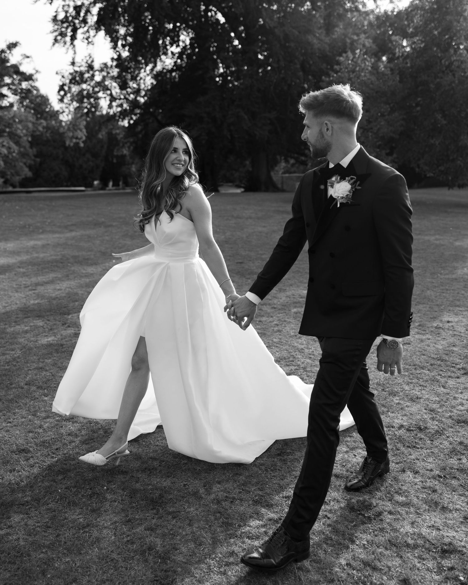 A couple walks hand in hand on their wedding day, with the bride in white gown and groom in black tuxedo.