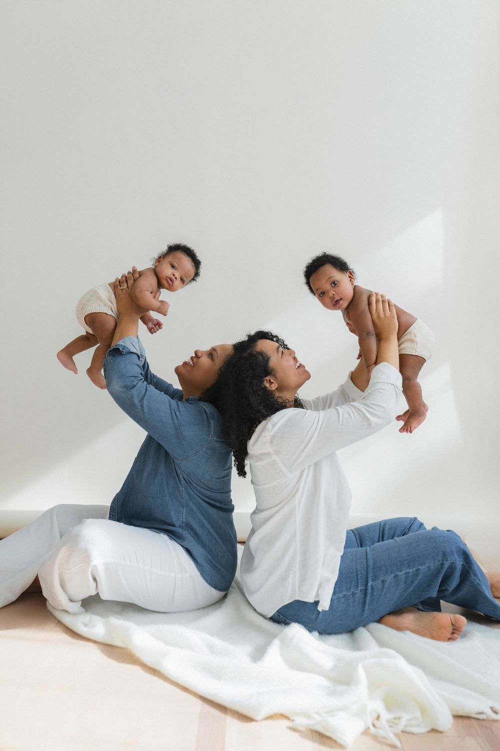 Joyful studio portrait showing playful moment lifting babies against white background.