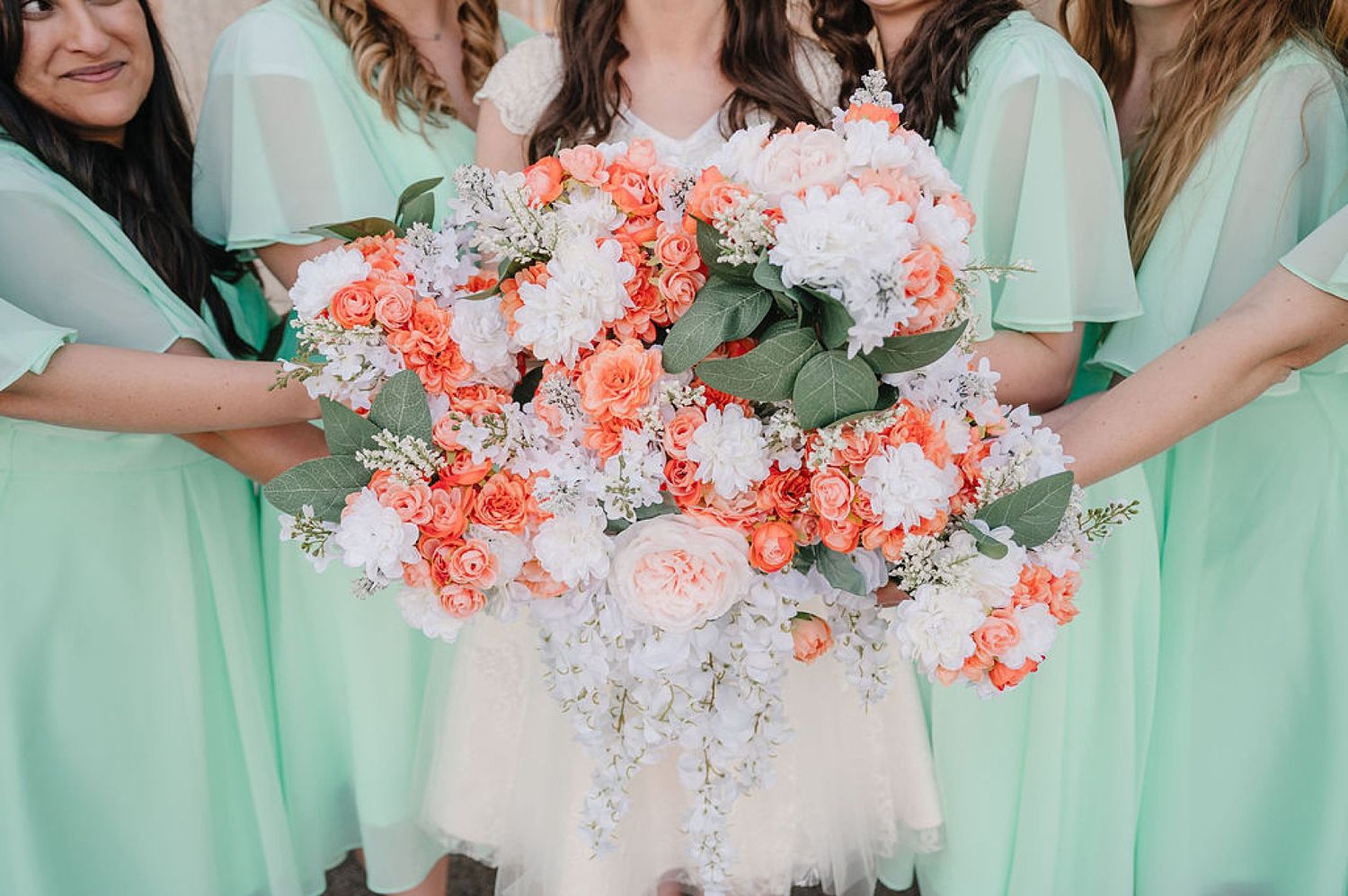 Close-up of coral and white wedding bouquets held against mint green bridesmaid dresses.