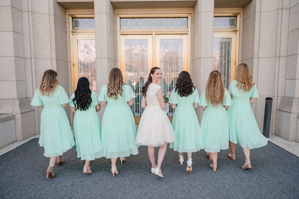Bridesmaids in matching mint green dresses pose with backs turned at an elegant stone entrance.