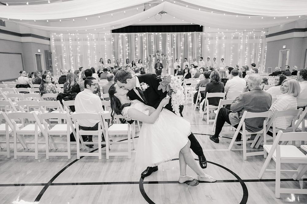 A romantic dip dance move by a couple during a wedding reception with guests seated in white chairs watching.