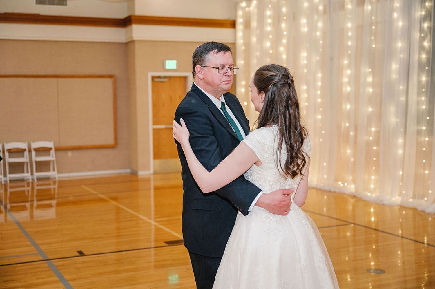 A father and daughter share a special dance moment at a wedding reception with twinkling lights in the background.
