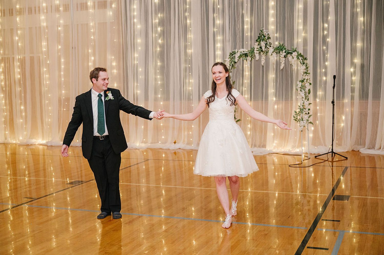 A couple performs a romantic dance together in a ballroom with beautiful curtain lights and floral decor.