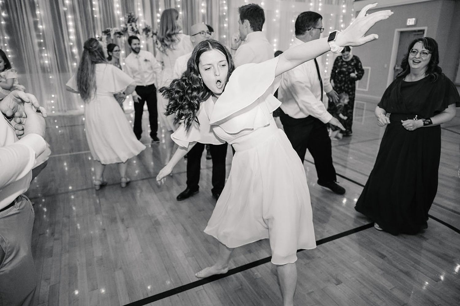 Wedding guests dancing and celebrating together in a venue with string lights on the walls.
