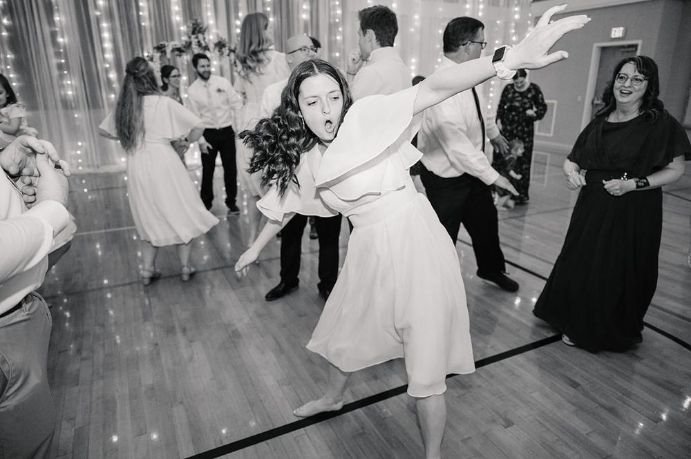 Wedding guests dancing and celebrating together in a venue with string lights on the walls.