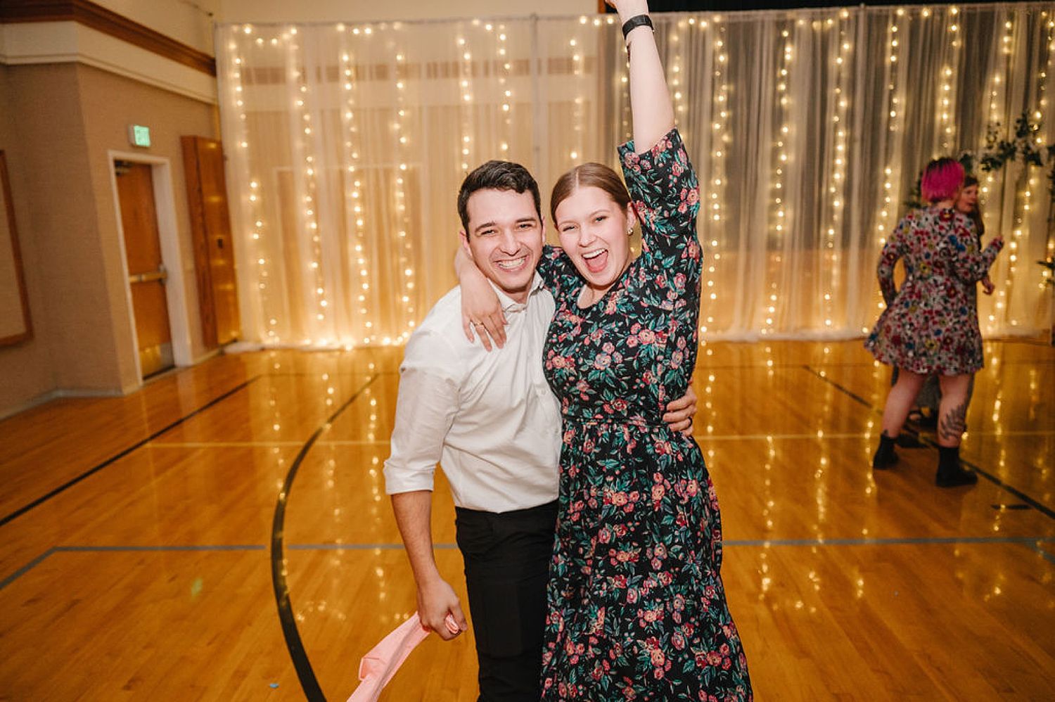 Two people dancing together at an event with twinkle lights and a wooden floor in the background.