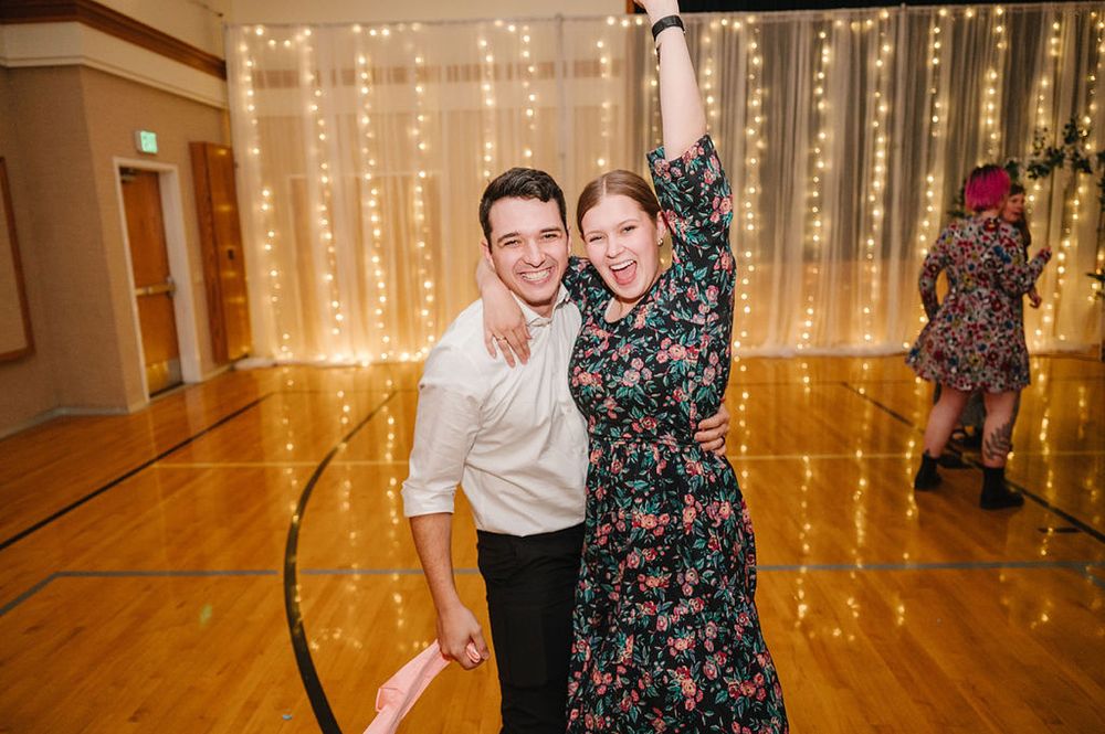 Two people dancing together at an event with twinkle lights and a wooden floor in the background.