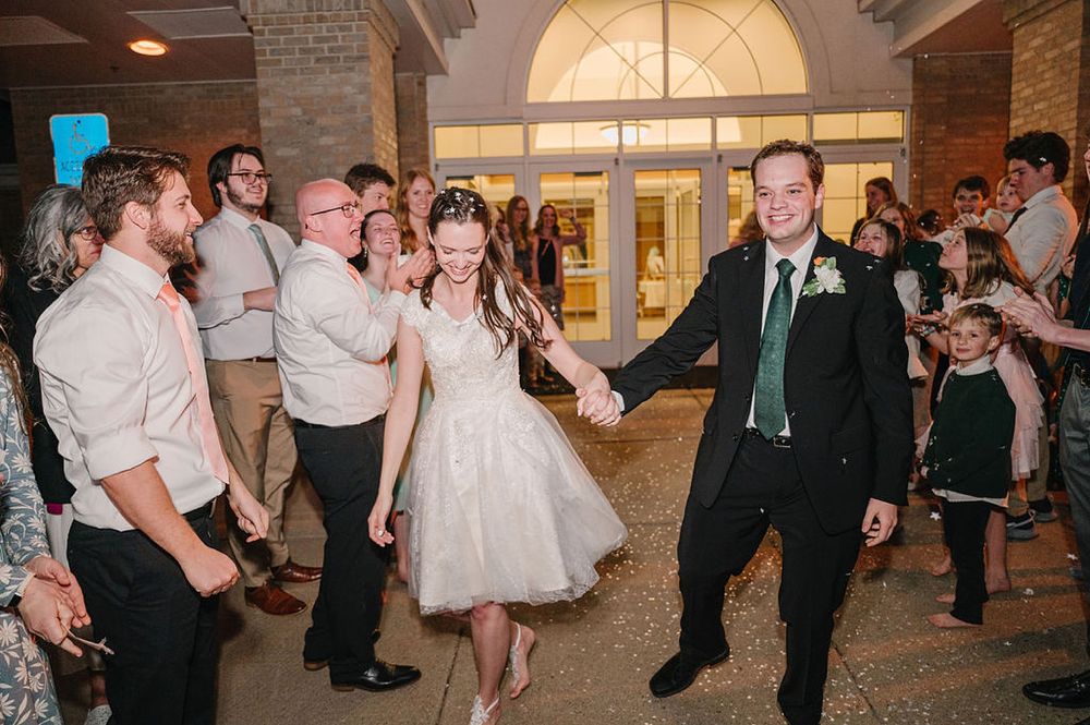 Wedding reception party in a grand venue shows couple dancing with guests watching and celebrating on the sidelines.