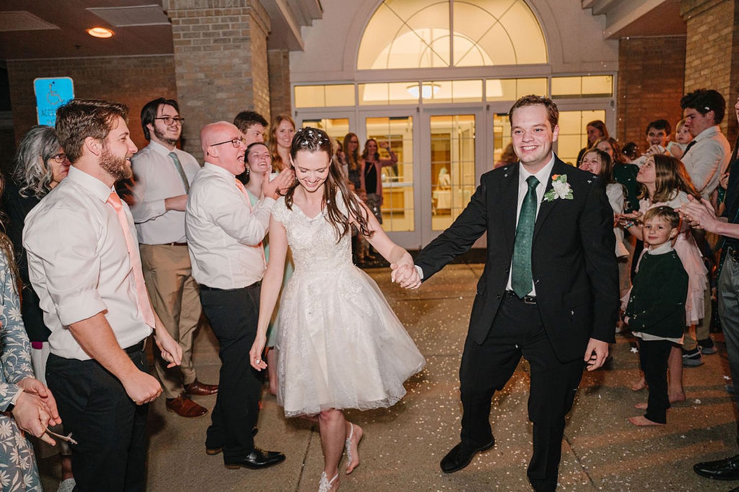 Wedding reception party in a grand venue shows couple dancing with guests watching and celebrating on the sidelines.