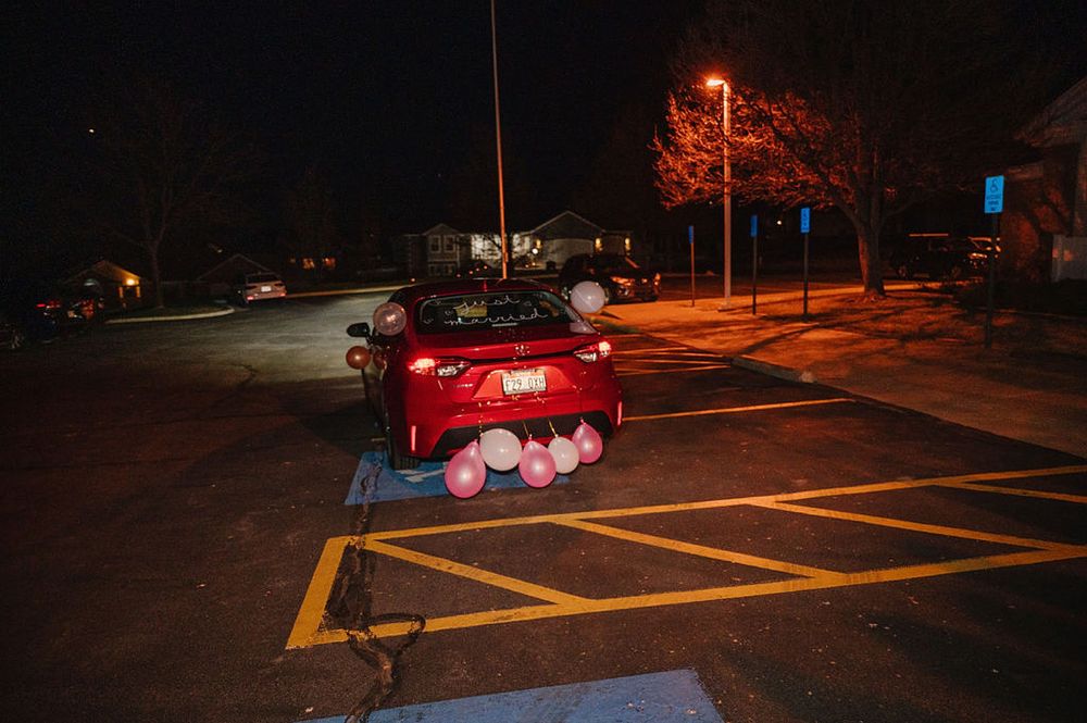 A red car parked in an illuminated parking lot at night with street lights glowing orange in the background.