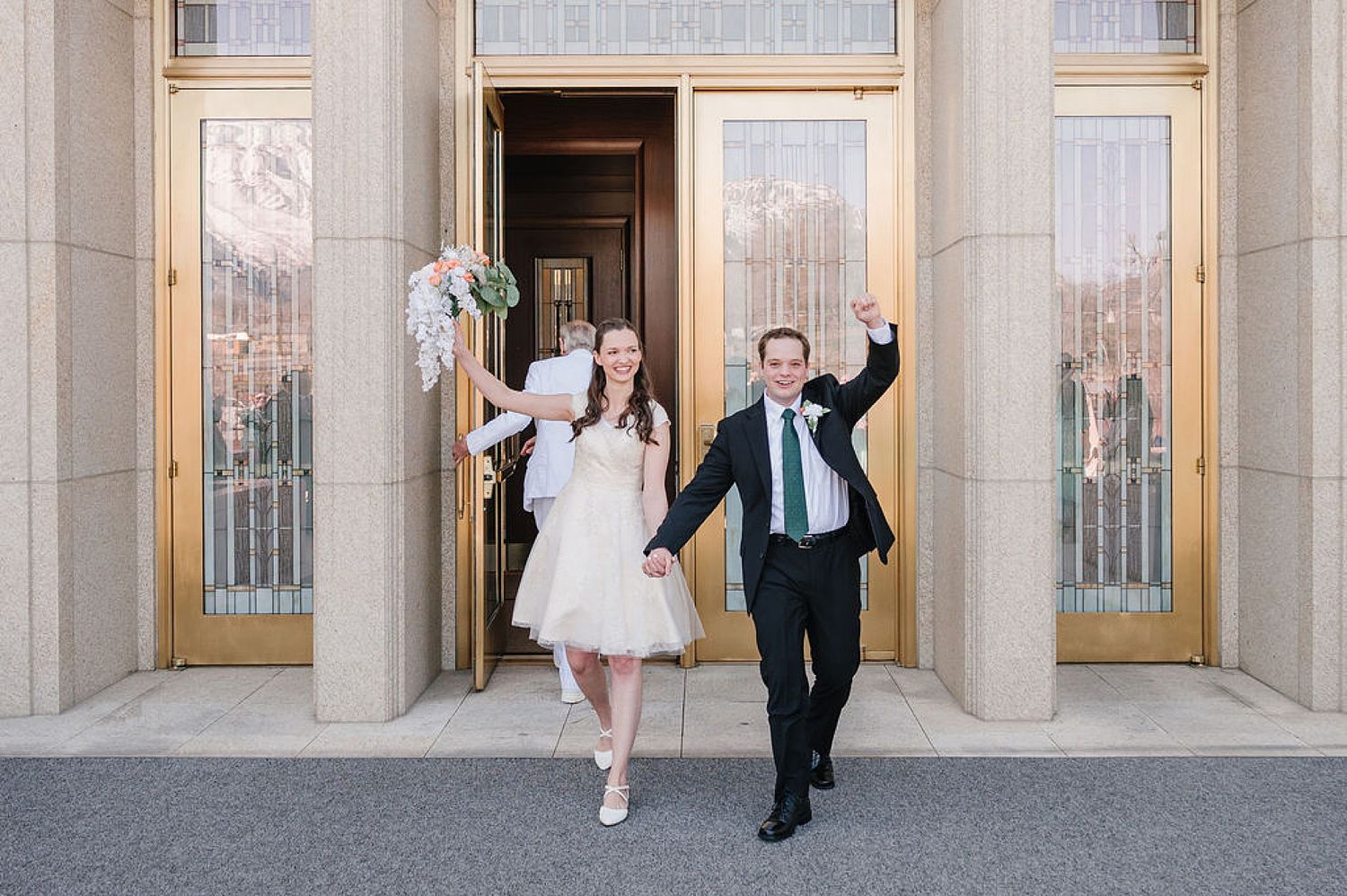 A joyful couple exits a temple building with grand columns and glass doors, celebrating their special day together.