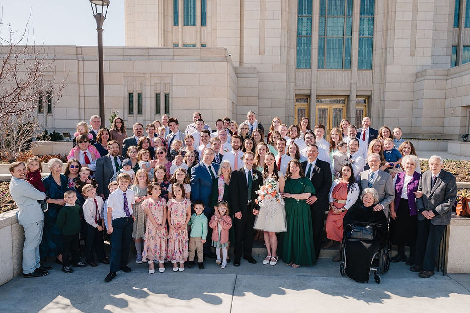 Large formal group photo of wedding guests gathered on steps outside a grand building with ornate architecture.