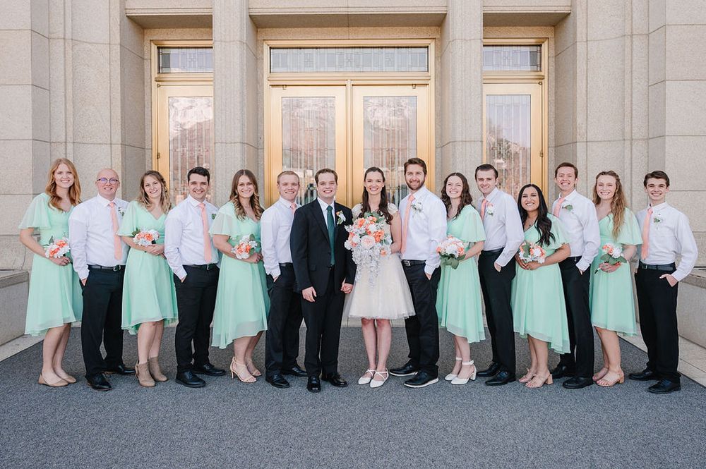 Wedding party in mint green and white formal attire poses together outside a grand building entrance.