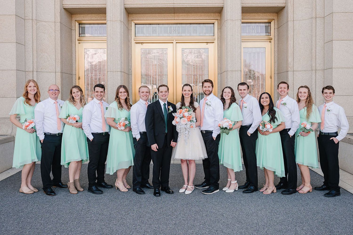 Wedding party in mint green and white formal attire poses together outside a grand building entrance.