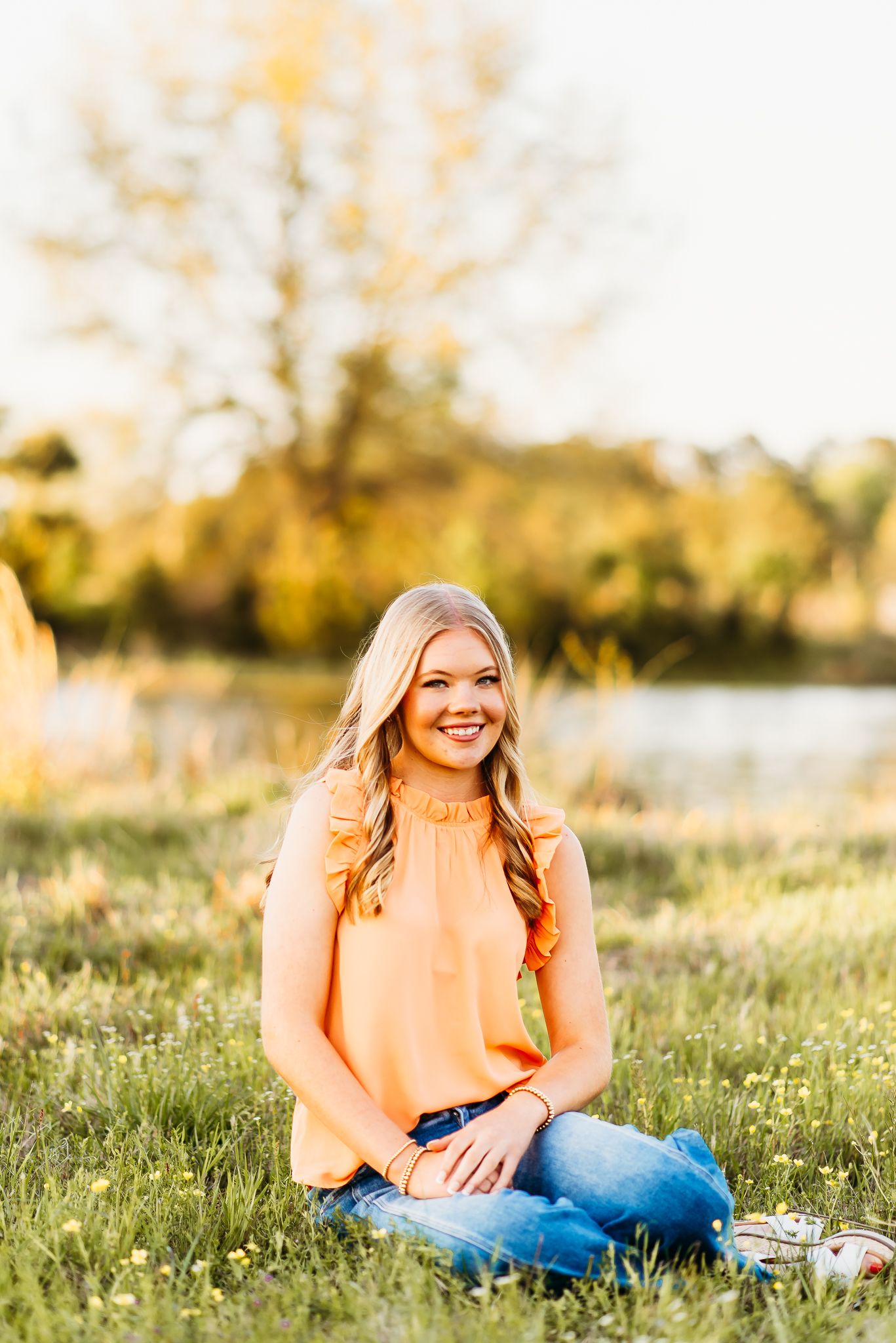 Woman in peach blouse sitting in sunny meadow during golden hour portrait session.