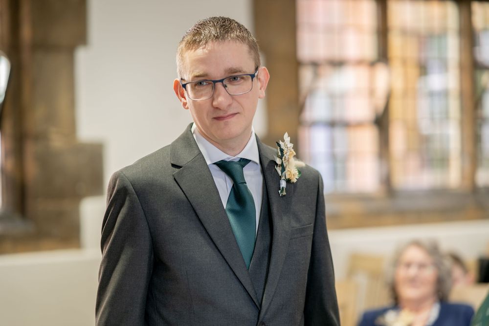 A groom in a grey suit and green tie stands at the altar.