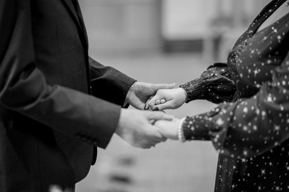 Black and white photo capturing a close-up of hands during a ring exchange ceremony.