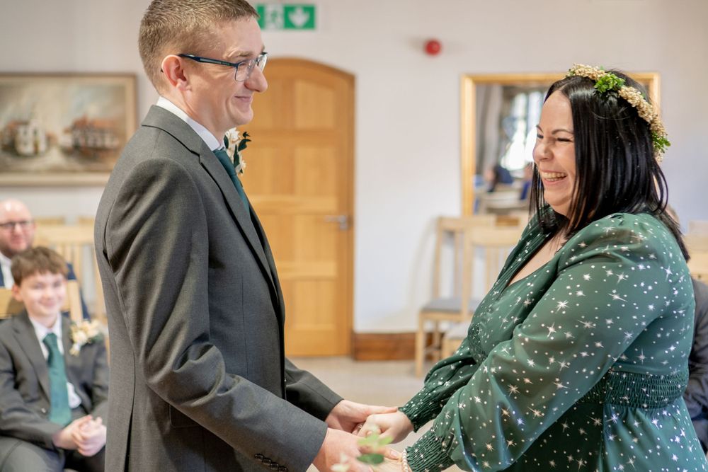 Couple holds hands during non-traditional wedding ceremony with bride wearing dark green patterned dress.