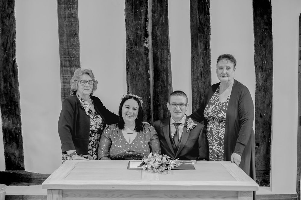 A black and white photograph showing a small group gathered around a table with wooden beams in the background.