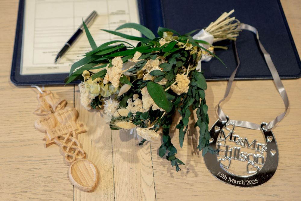 A wilted floral arrangement with pale blooms lies on a desk next to some paperwork and decorative items.