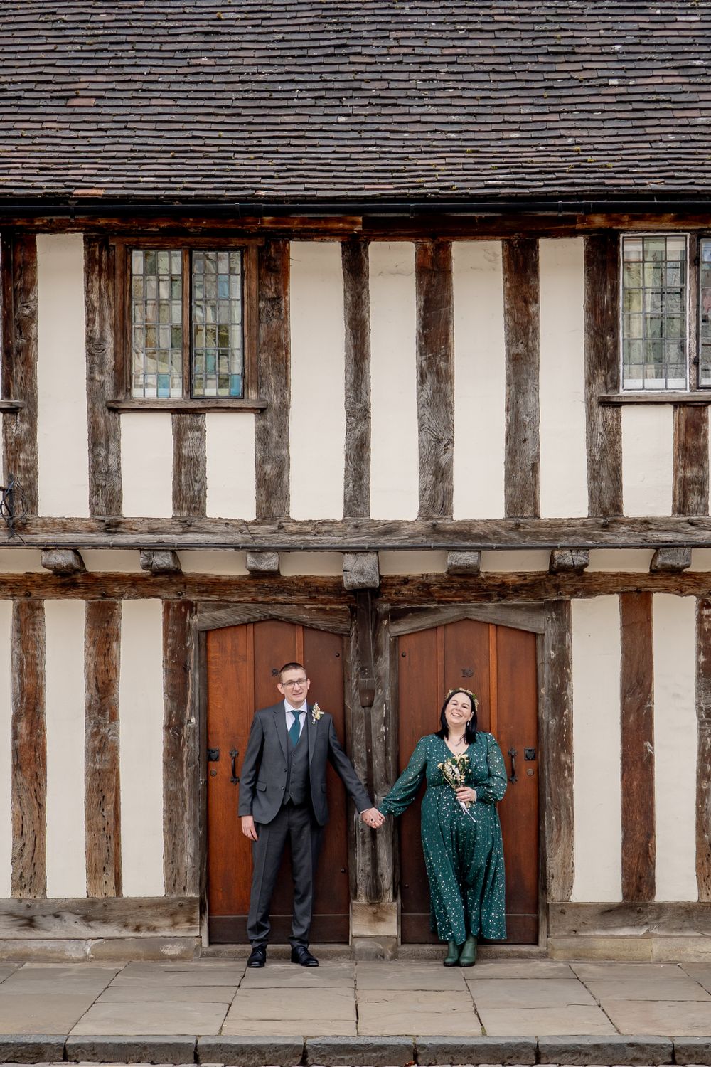 Couple poses in front of a historic Tudor-style building with timber framing and white walls.