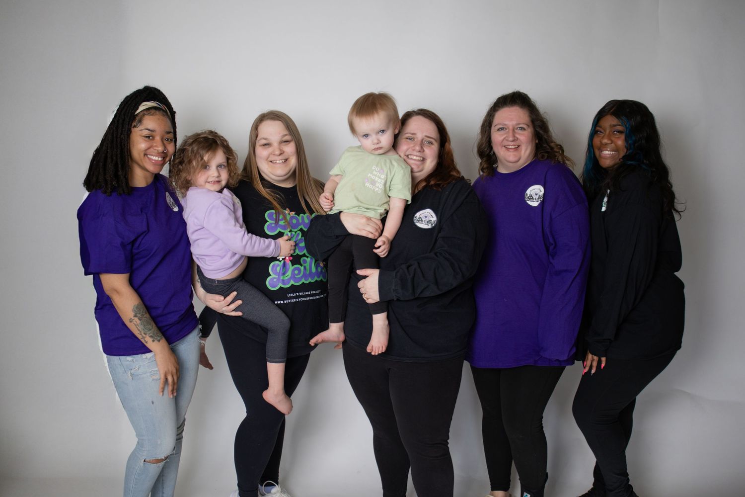 Group of people wearing purple shirts posing together against grey background.