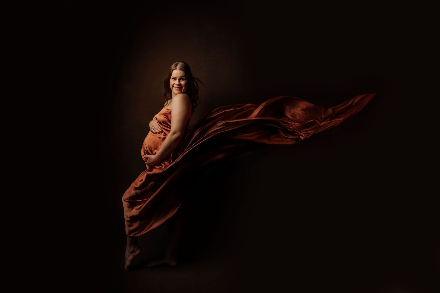 Artistic maternity silhouette with flowing fabric against dark background.