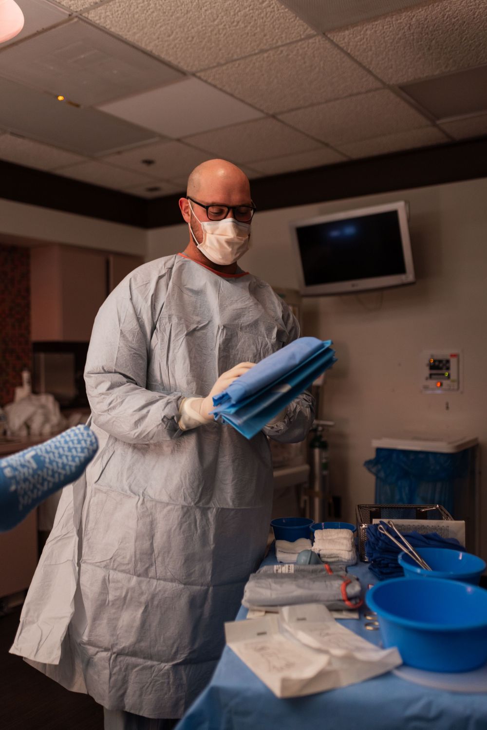 Medical professional in protective gear handling surgical supplies in a hospital room.