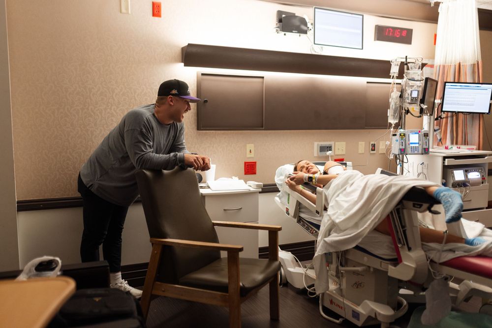 A person leans over a hospital bed while monitoring medical equipment in a patient room.