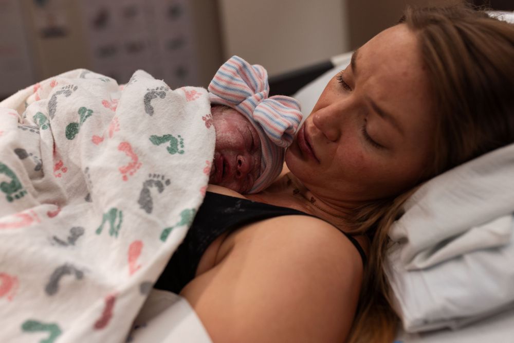 Newborn baby wrapped in patterned blanket resting on parent's chest.