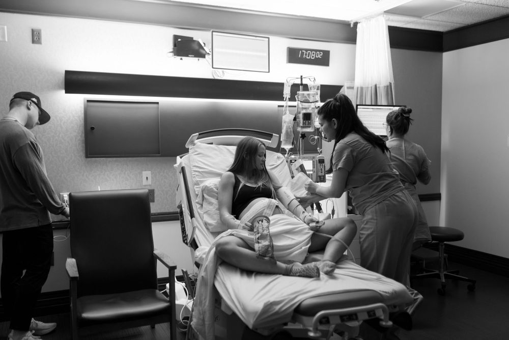 Medical staff assist during a childbirth procedure in a monochrome hospital room setting.