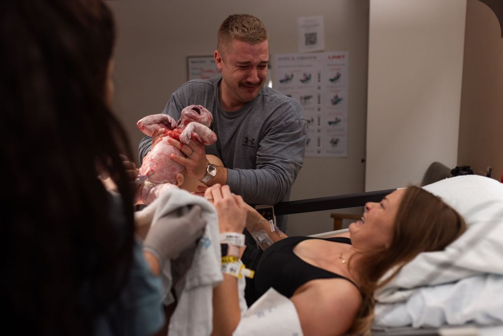 A newborn baby being held carefully in a hospital room while surrounded by family.