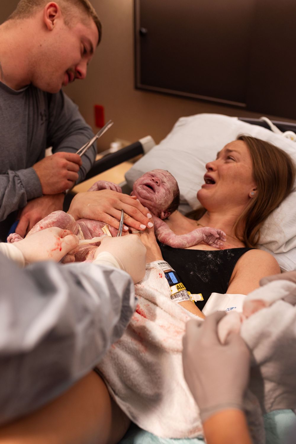 A newborn baby emerges during a hospital birth with medical staff assisting.