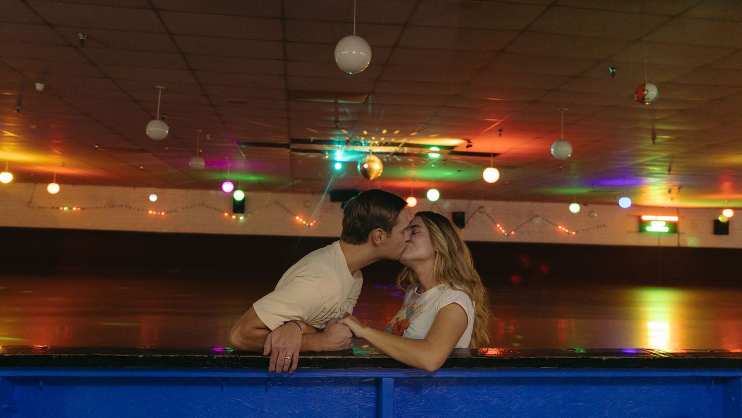 A couple shares a romantic moment at a bowling alley with colorful lights glowing in the background.